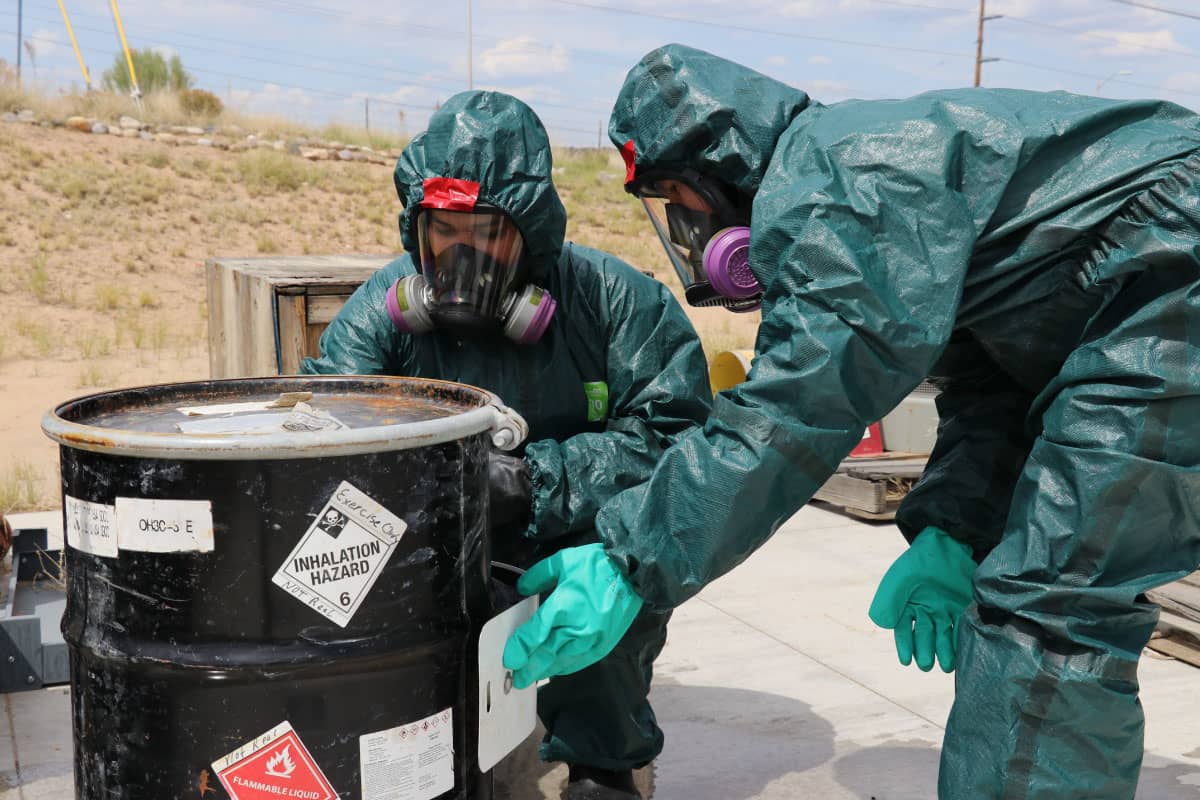 Two people, dressed in hazmat suits handle hazardous waste material.