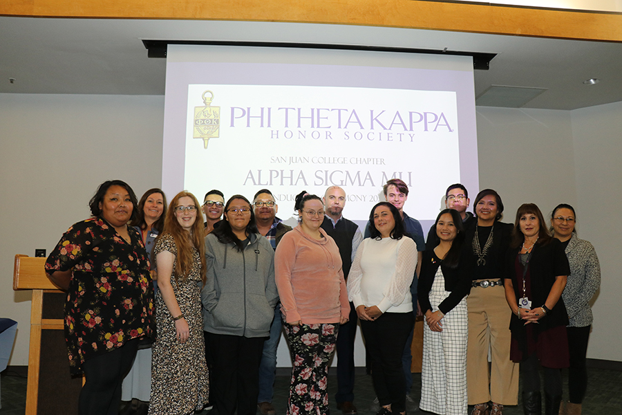 Members of Phi Theta Kappa standing in front presentation slide with Phi Theta Kappa Honor Society information