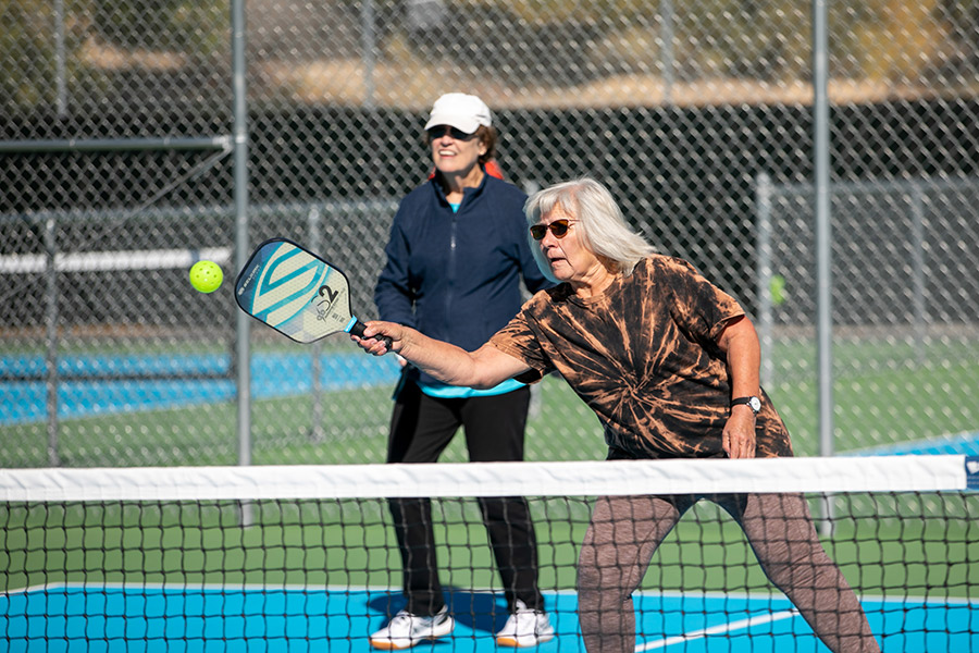Female returns a serve playing Pickleball with her teammate at outdoor pickleball courts at Farmington's Brookside Park.
