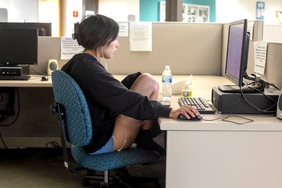 Female student sitting at desk with earbuds in working on caomputer