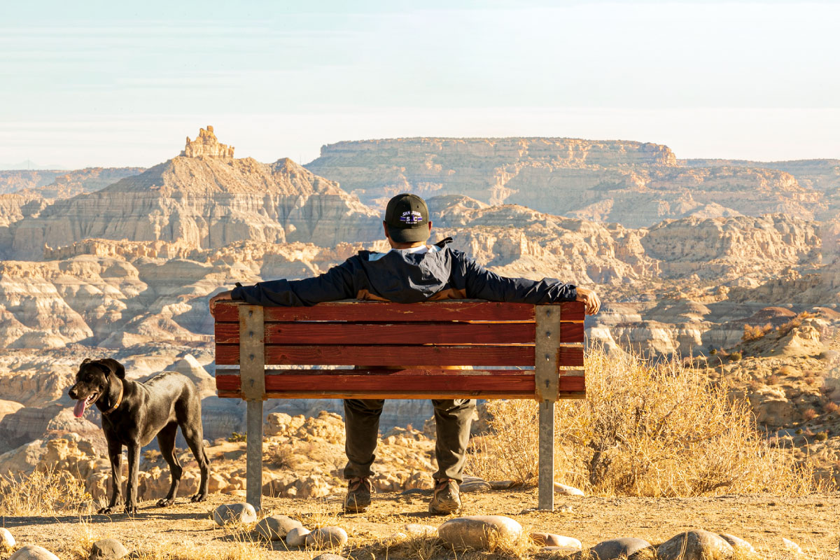 Black dog and person sitting on bench looking at Angel Peak