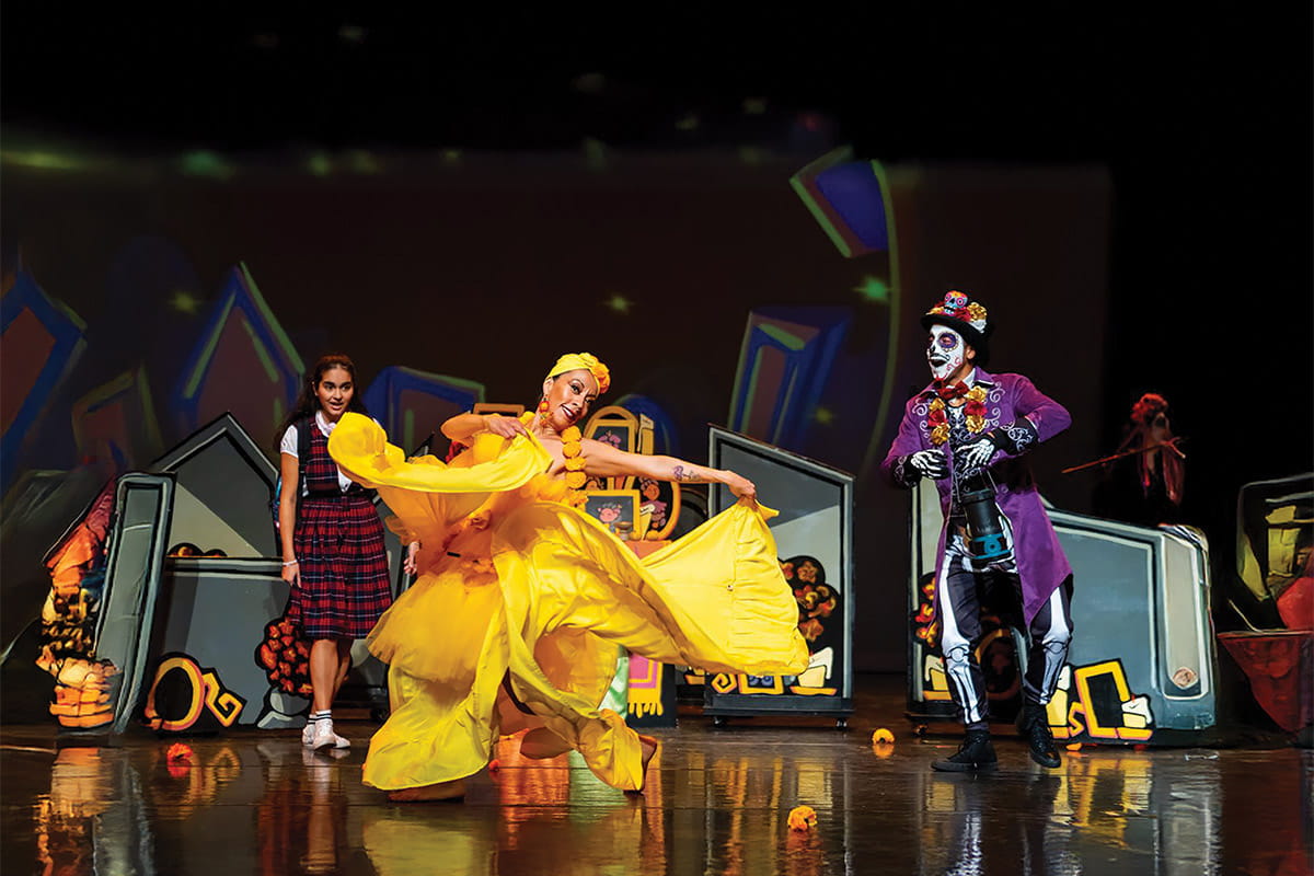 A group of performers dancing in gold dresses with dia de los muertos skull makeup