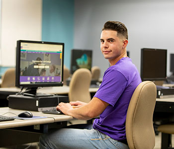 Person wearing purple shirt, sitting a computer.
