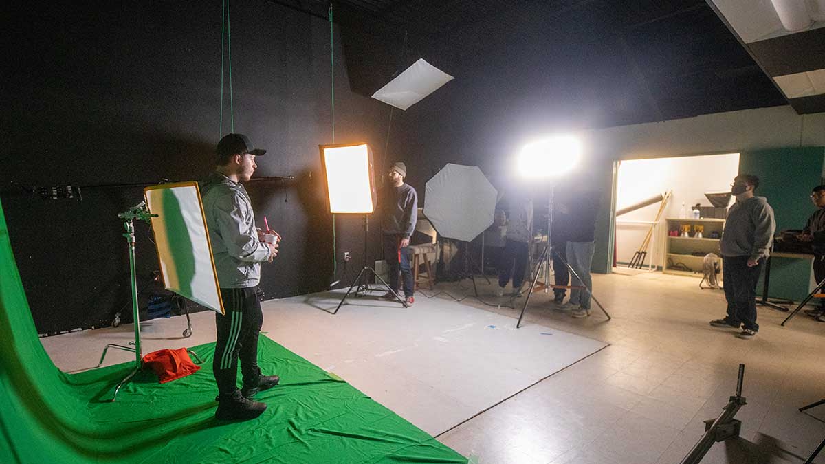 Students standing in front of a green screen with film equipment.