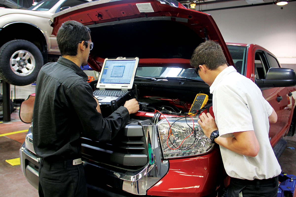 Two students looking under the hood of a pickup.