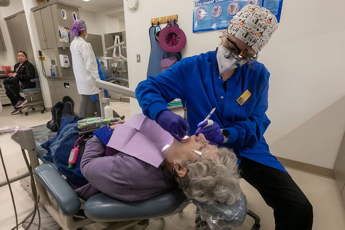 A student hygienist examines the mouth of a woman laying in a dental chair