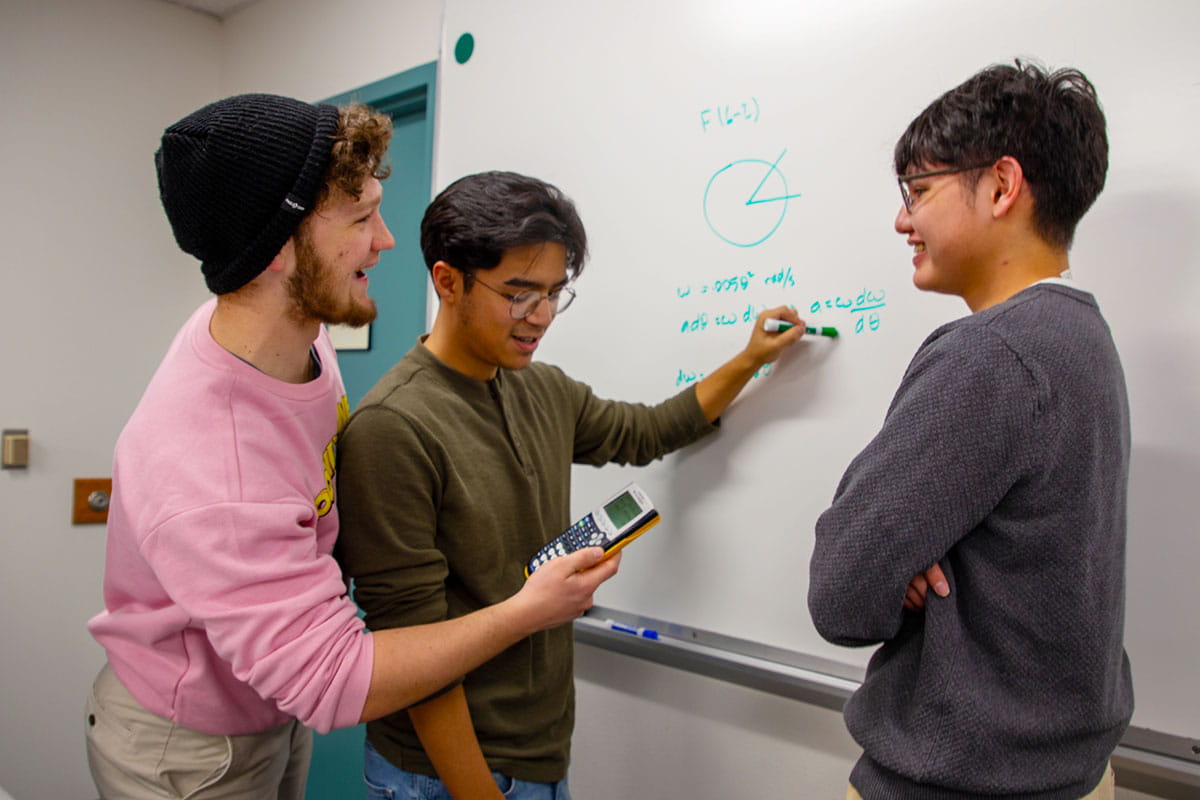 Three San Juan College students working on a math problem on a whiteboard