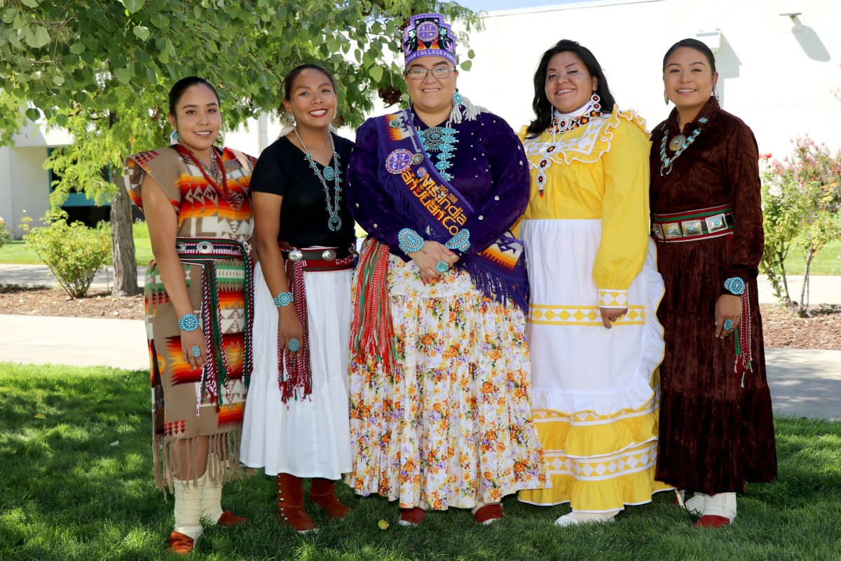 Five individuals pose and smile while wearing native-style dress