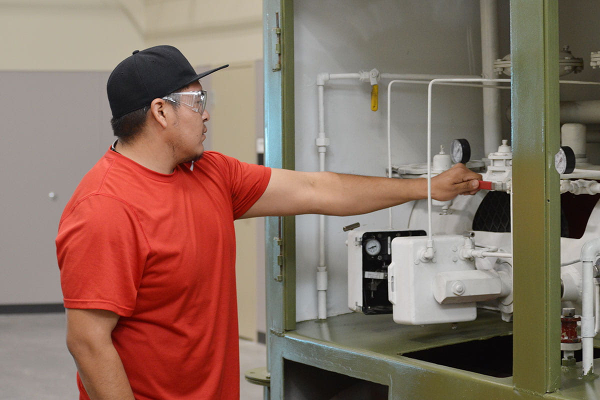 An individual wearing a hat and safety goggles turns the valve on production machinery