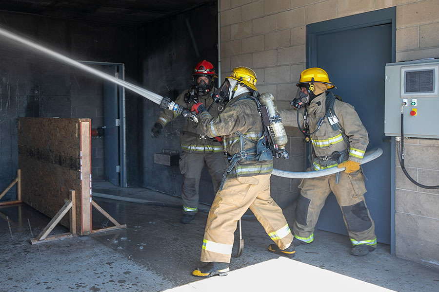 Three students with firefighter equipment spraying out fire