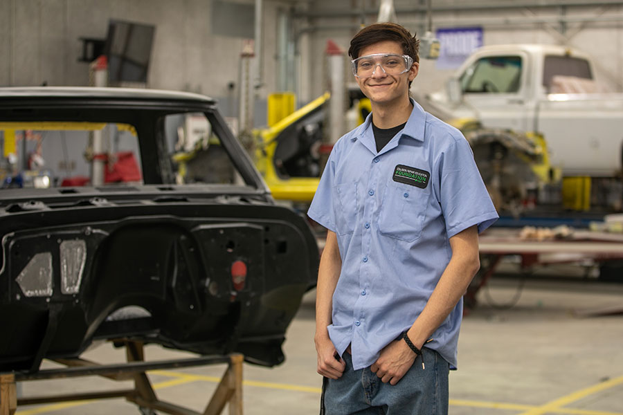 San Juan College student standing in front of a car frame in the auto body shop