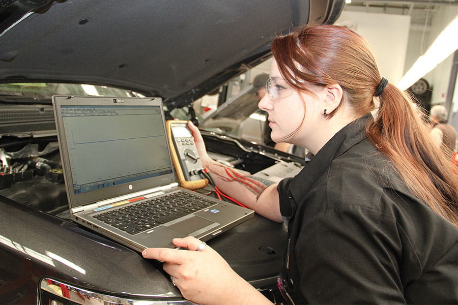 San Juan College student using a diagnostic tool and laptop on a car