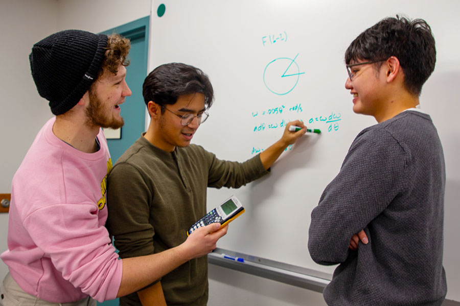 Three San Juan College students working on a math problem on a whiteboard