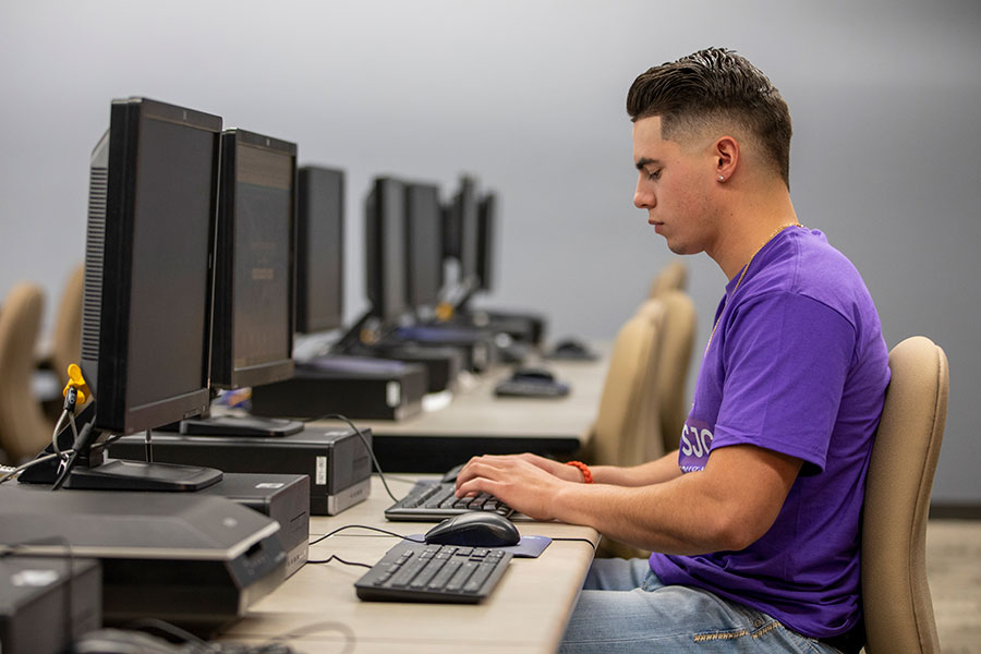 An individual wearing a purple shirt sits at a computer, typing on the keyboard