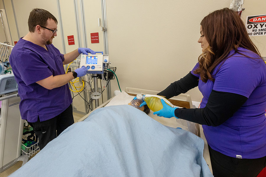 Two RT students demonstrate skills on a dummy in a hospital bed