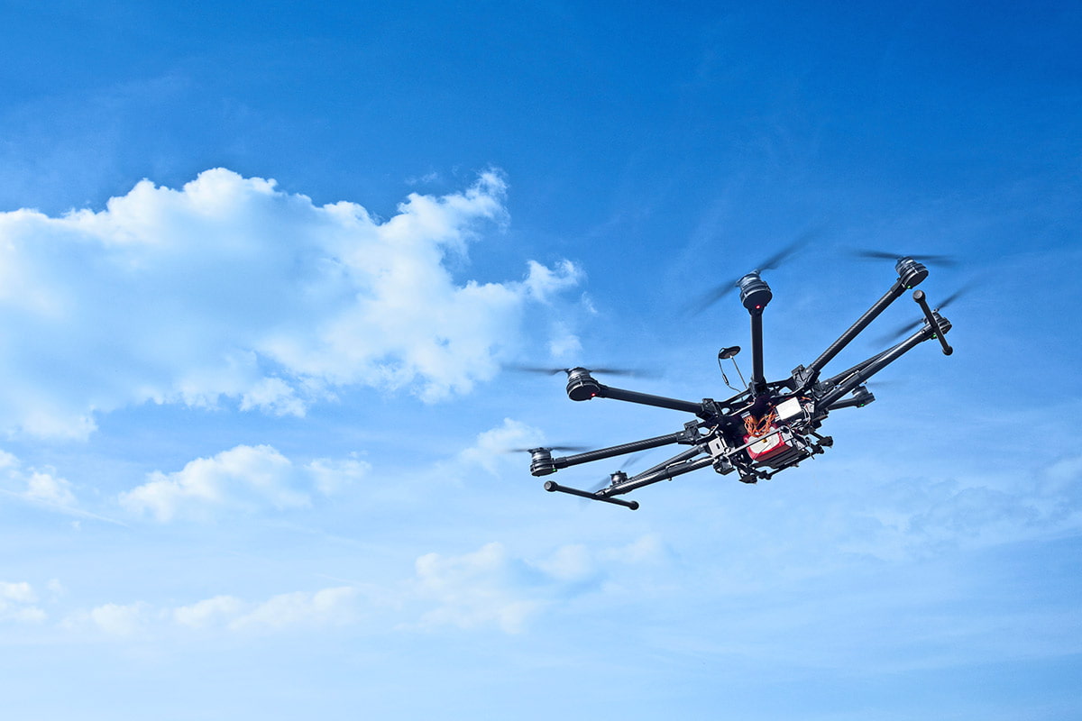 octocopter flies high with bright blue sky and clouds in the background.