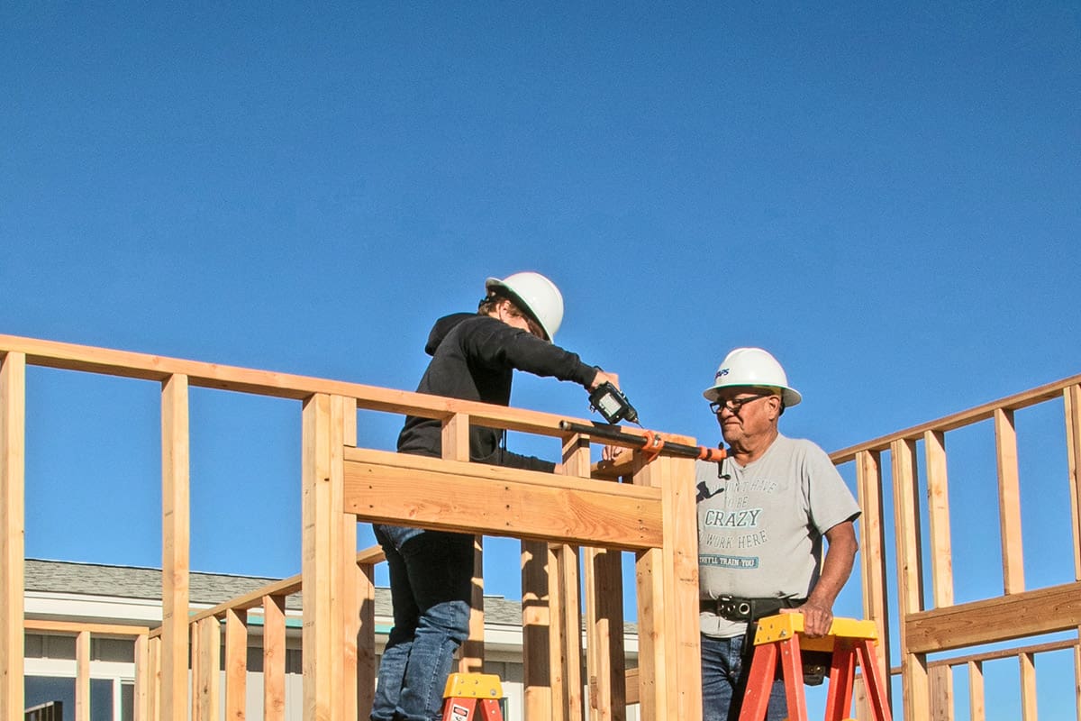 intern on a construction job site receives instruction from mentor on house framing.