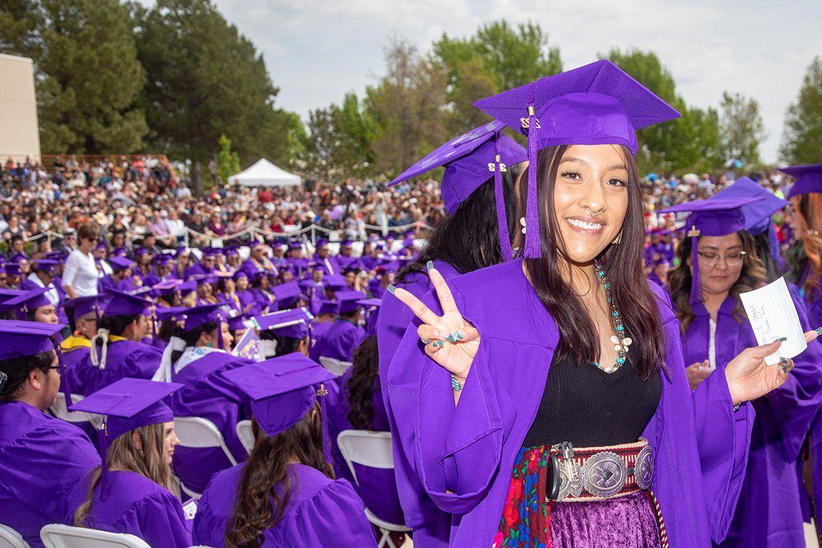 female native graduate smiles and flashes a peace sign at graduation