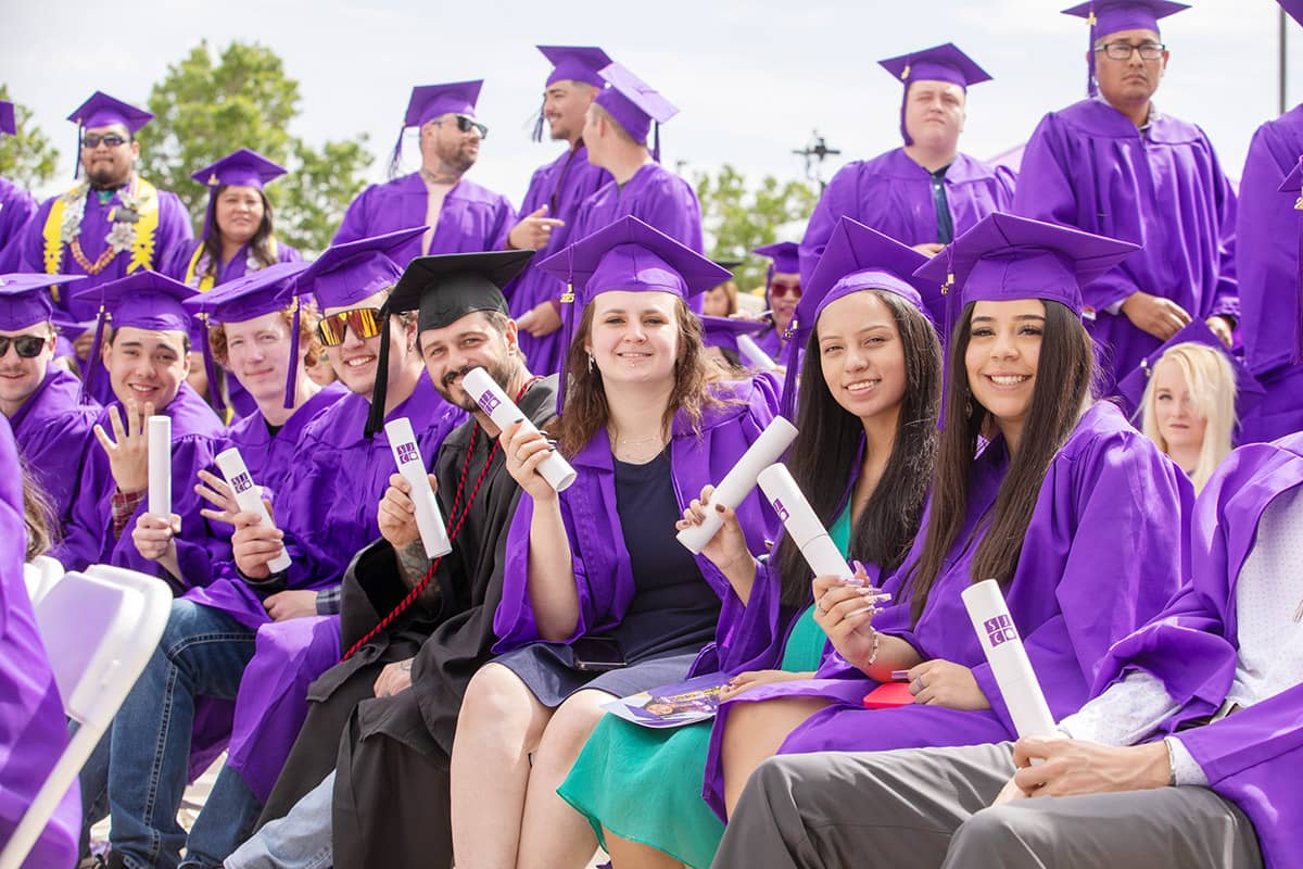 Smiling SJC Graduates wearing cap and gown at graduation.