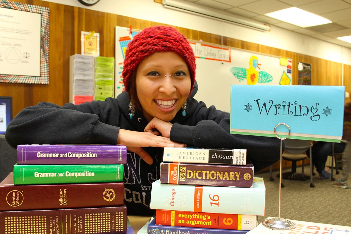 Smiling student in the Tutoring Center with variety of text books.