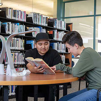 Two students sitting at a table reading a book in the SJC Library